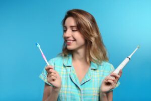 Young,Woman,Choosing,Between,Manual,And,Electric,Toothbrushes,On,Color